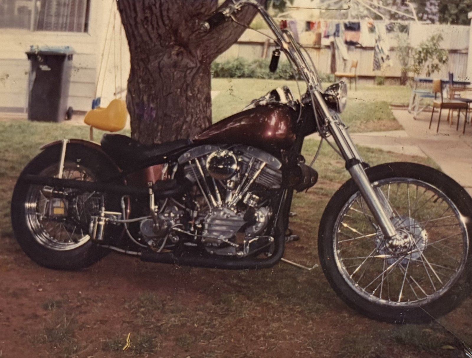 Dicko's Harley-Davidson chopper, maroon tank and chrome engine, parked on a lawn. Scanned from an old print